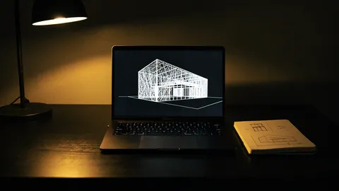 Illustration: A slim black laptop glowing with a fine wireframe mesh of a building on a dark desk.