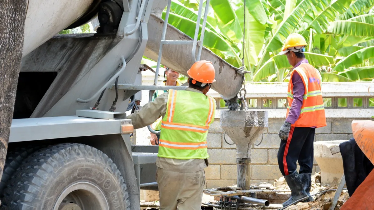 Workers pouring wet concrete into formwork on a site.