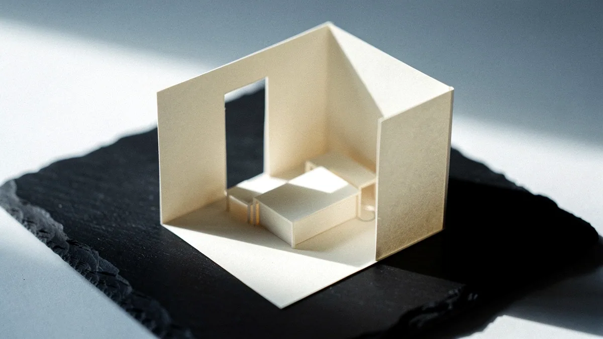 Illustration: A small isometric paper room model standing on a black slate slab.
