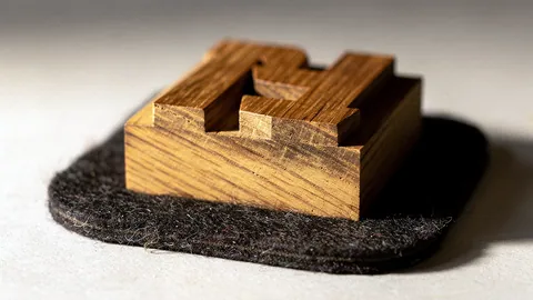 Illustration: A carved oak wood type block with a bold geometric letterform cut into its top.