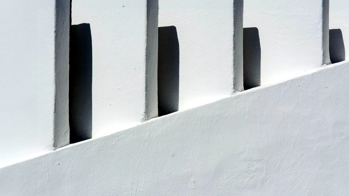 Sharp geometric shadows falling across a plain white wall.