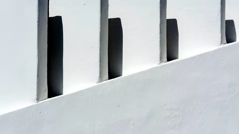 Sharp geometric shadows falling across a plain white wall.