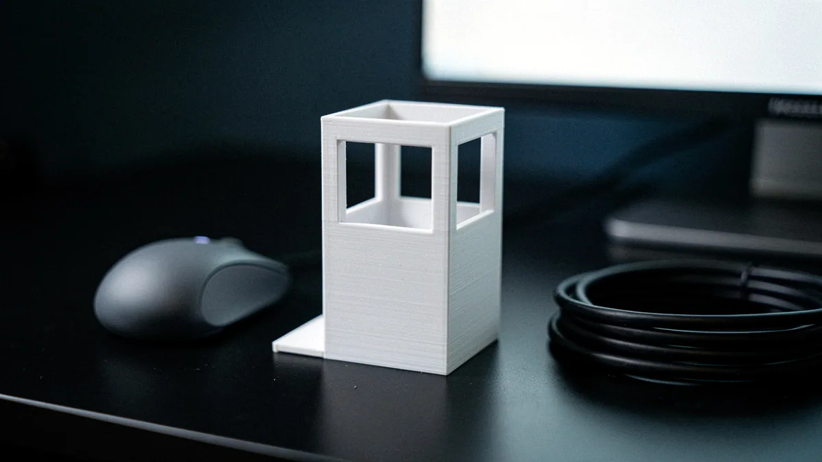 Illustration: A small white 3d printed building model on a black desk beside a grey mouse.