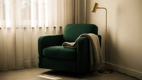 Illustration: A deep green fabric reading armchair in a window alcove with a brass floor lamp.