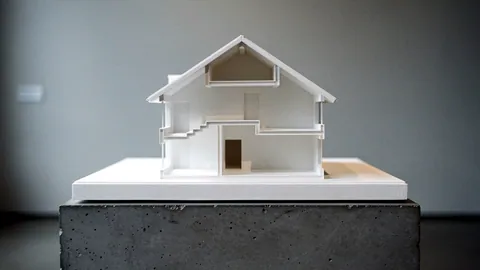 Illustration: A white plaster house cross section cast with stepped room volumes on a concrete plinth.
