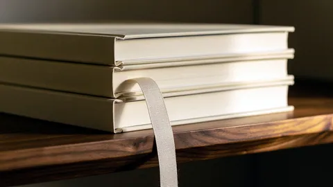 Illustration: A neat stack of blank cream hardcover books with a linen ribbon on a walnut shelf.